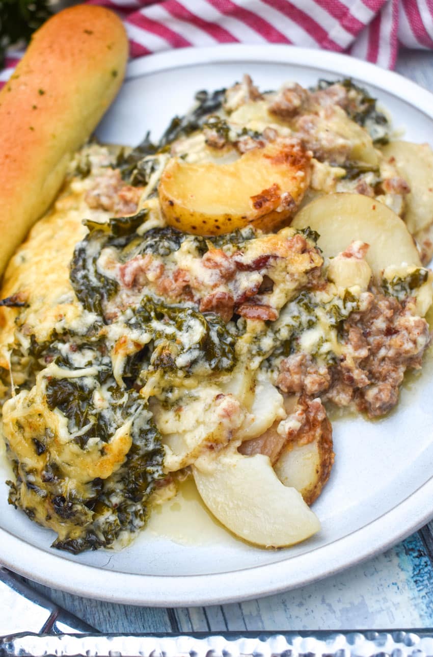 zuppa toscana casserole on a white dinner plate with a breadstick on the side