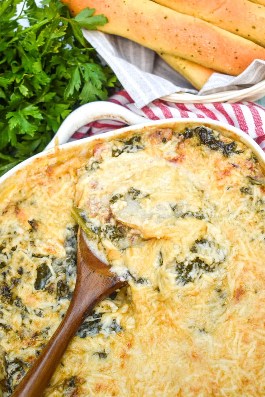 a wooden spoon scooping zuppa toscana casserole out of a white baking dish
