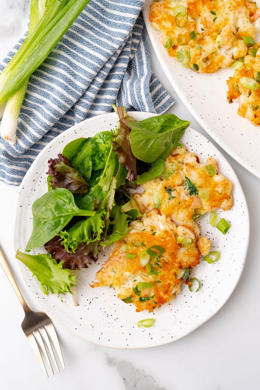 fried shrimp fritters on a white platter with a small bowl of cocktail sauce on the side