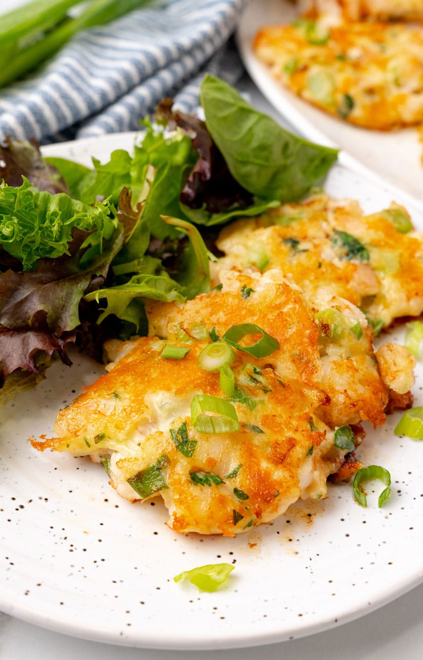 fried shrimp fritters on a white platter with a small bowl of cocktail sauce on the side