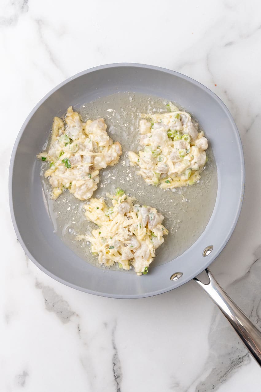 three shrimp fritters frying in a small gray skillet