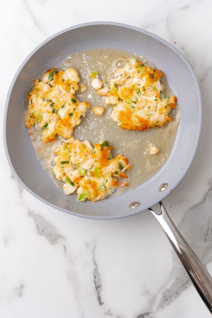 three shrimp fritters frying in a small gray skillet