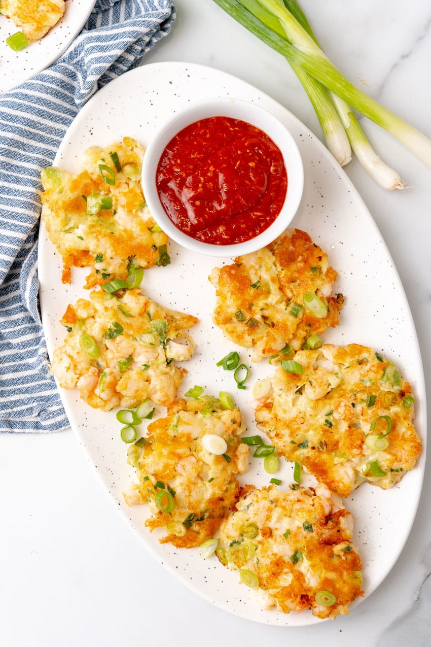 fried shrimp fritters on a white platter with a small bowl of cocktail sauce on the side