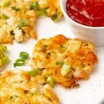 fried shrimp fritters on a white platter with a small bowl of cocktail sauce on the side