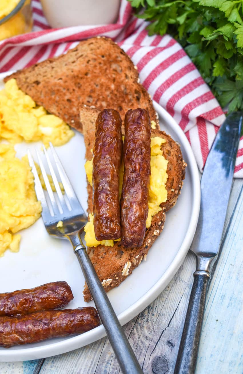 two air fried sausage links over scrambled eggs on a slice of toast resting on a white plate