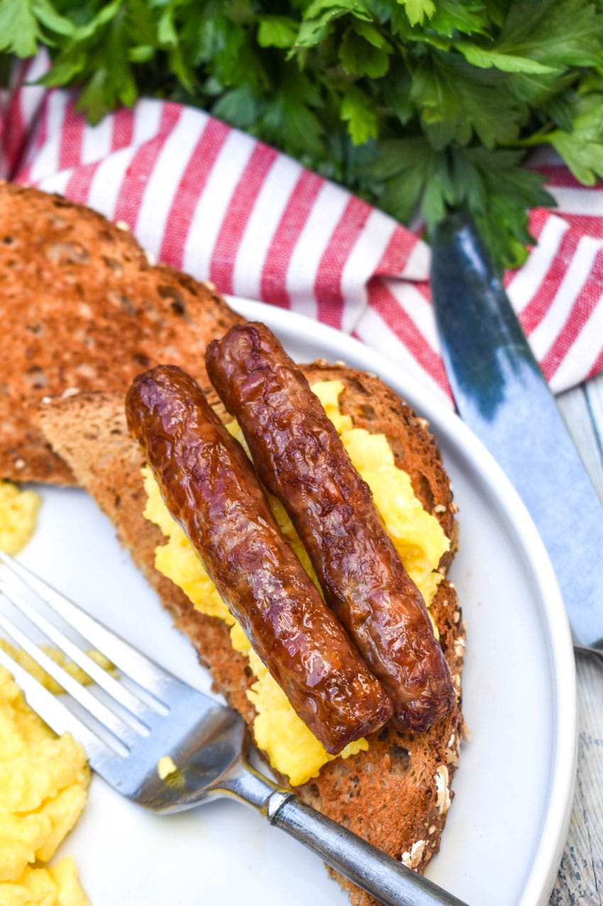 two air fried sausage links over scrambled eggs on a slice of toast resting on a white plate