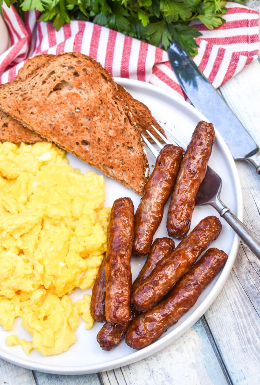 air fryer breakfast links on a white plate with scrambled eggs and toast on the side