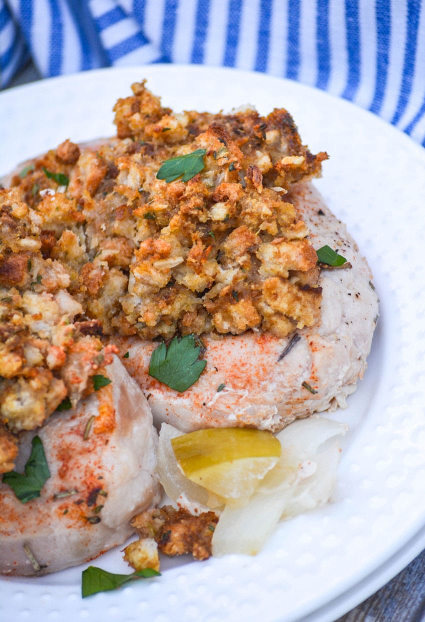 stuffing topped baked pork chops over a mixture of apples onions and potatoes on a white plate