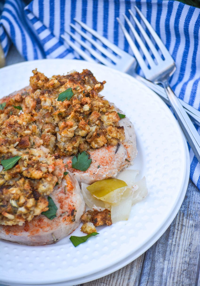 stuffing topped baked pork chops over a mixture of apples onions and potatoes on a white plate