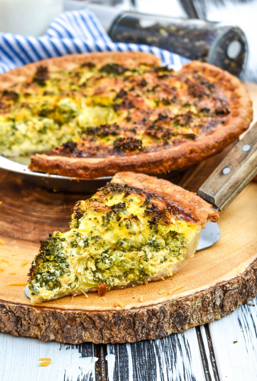 a slice of broccoli cheddar quiche resting on a wooden cutting board