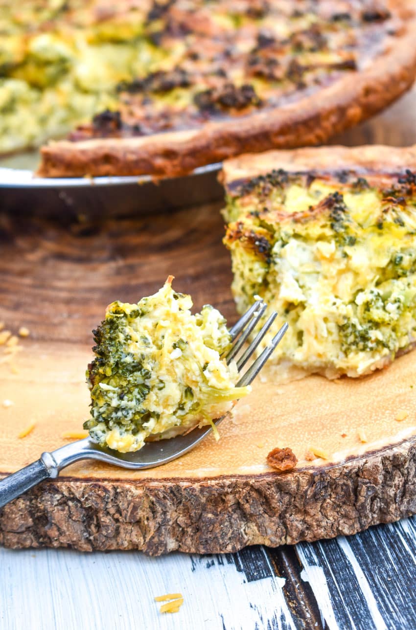 a slice of broccoli cheddar quiche resting on a wooden cutting board