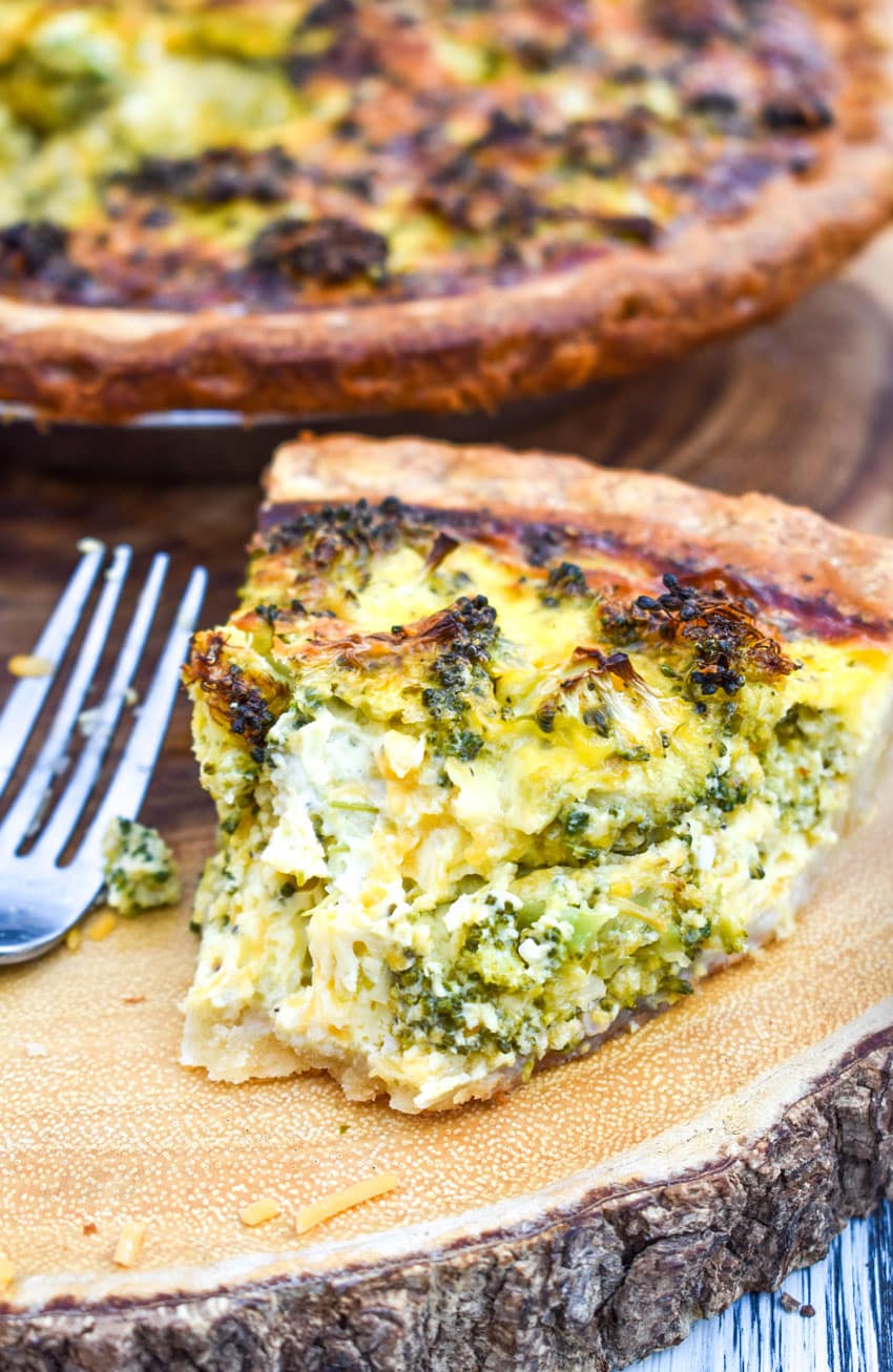 a slice of broccoli cheddar quiche resting on a wooden cutting board