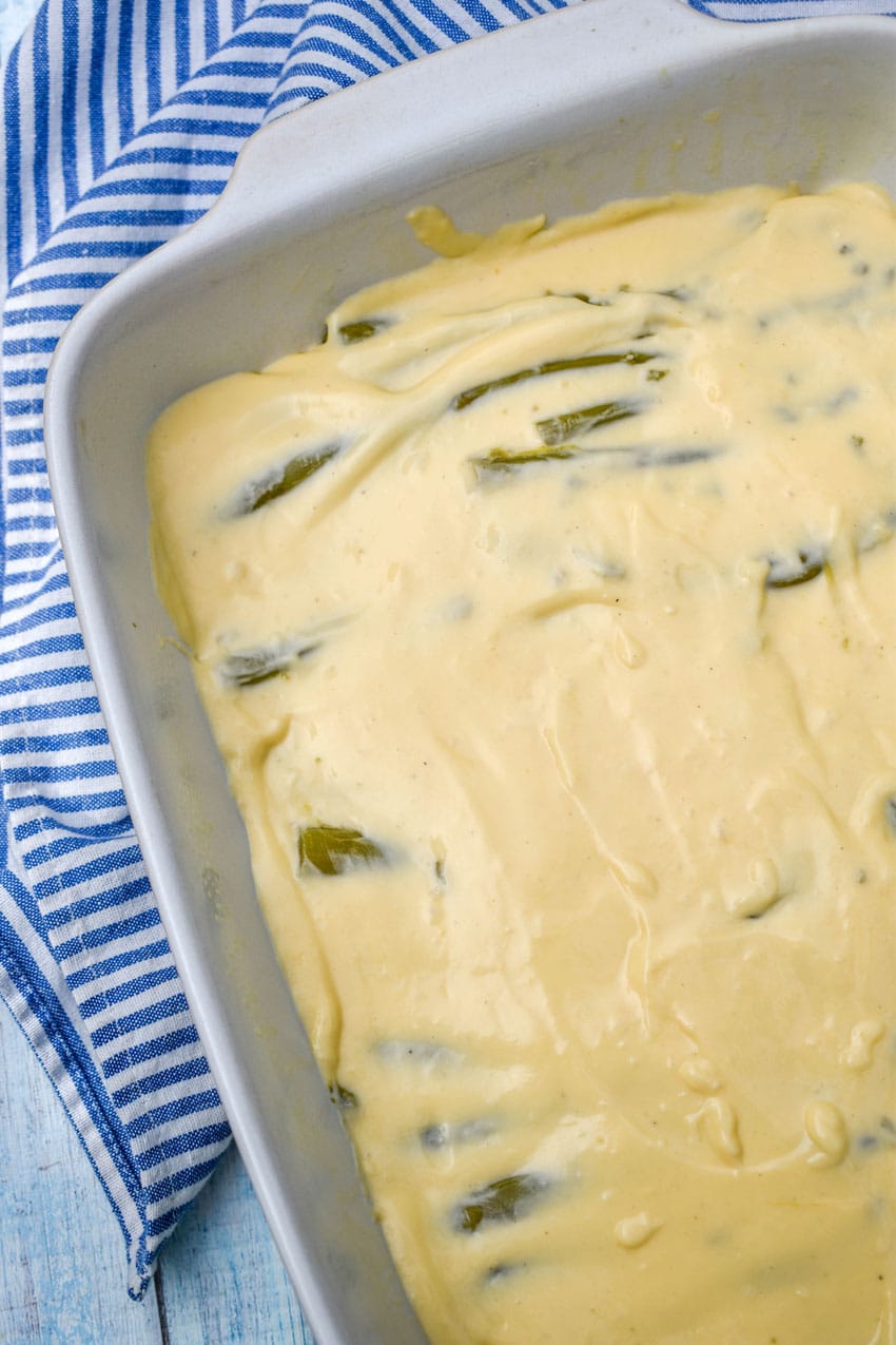 cheese sauce spread evenly out overtop of canned asparagus spears in a white baking dish