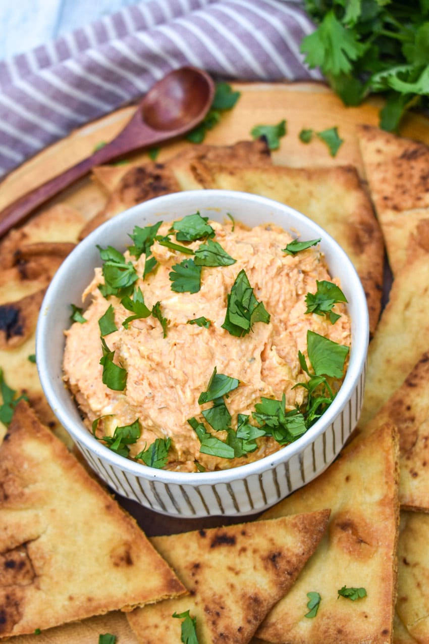 chicken tikka masala dip in a small white bowl surrounded by baked naan bread chips