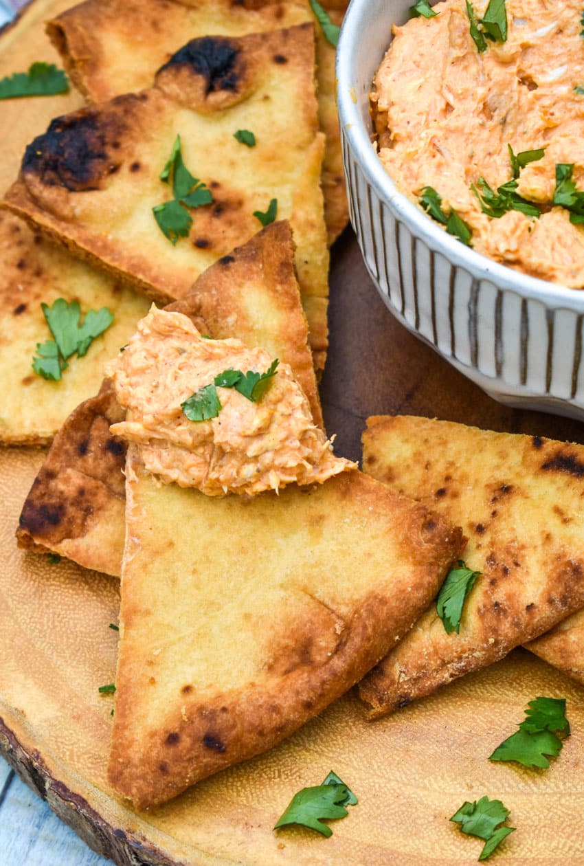 a baked naan chip topped with chicken tikka masala dip resting on a wooden cutting board