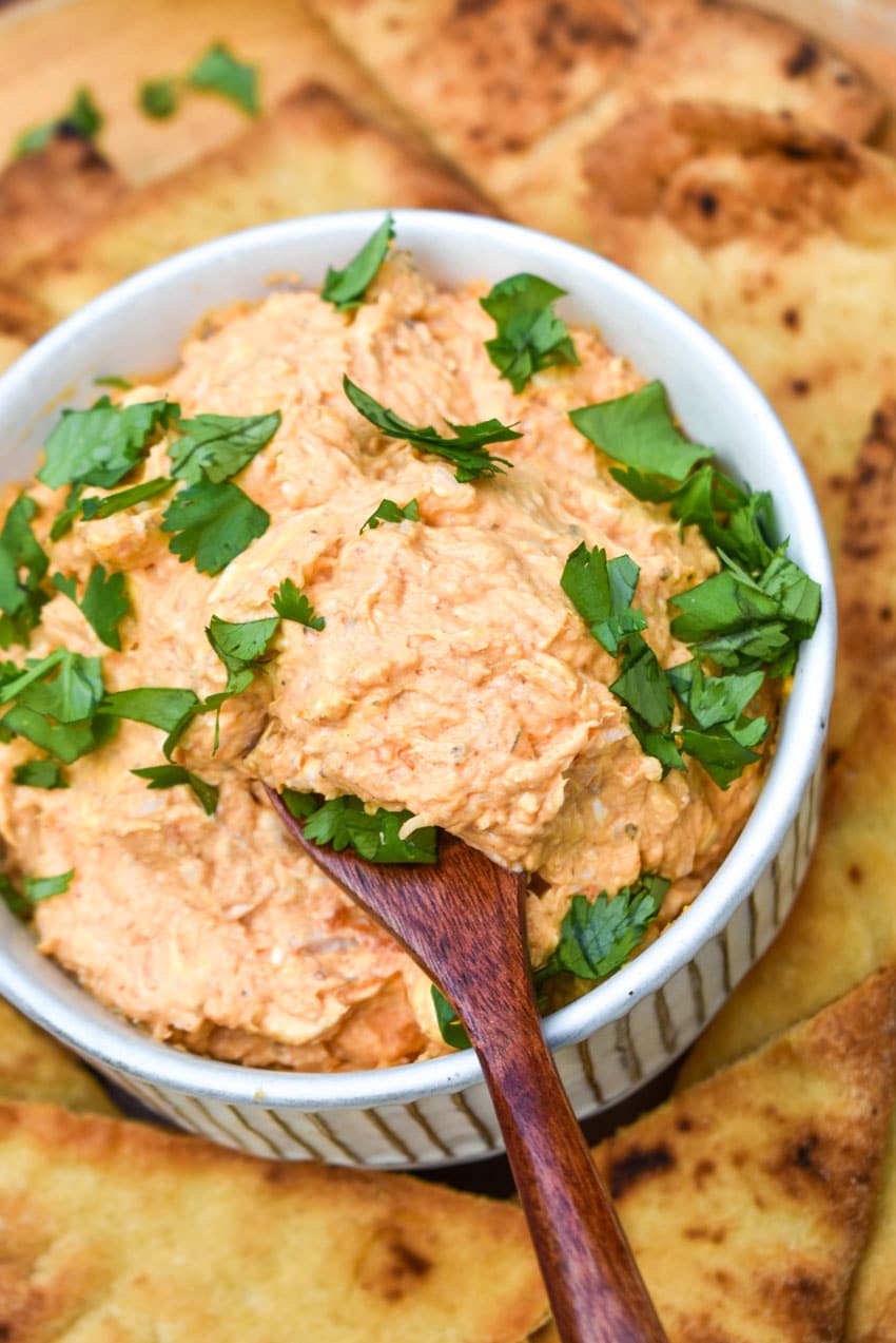 a wooden spoon scooping chicken tikka masala dip out of a small white bowl