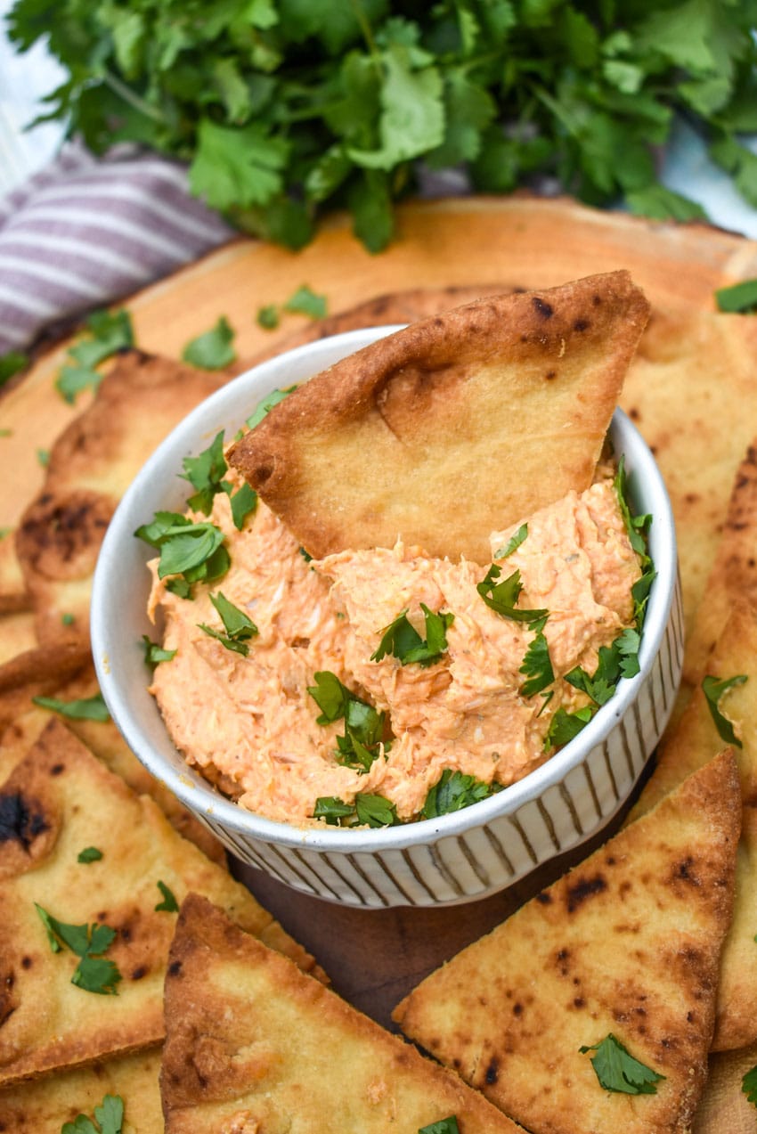 a baked naan bread chip scooping chicken tikka masala dip out of a small white bowl