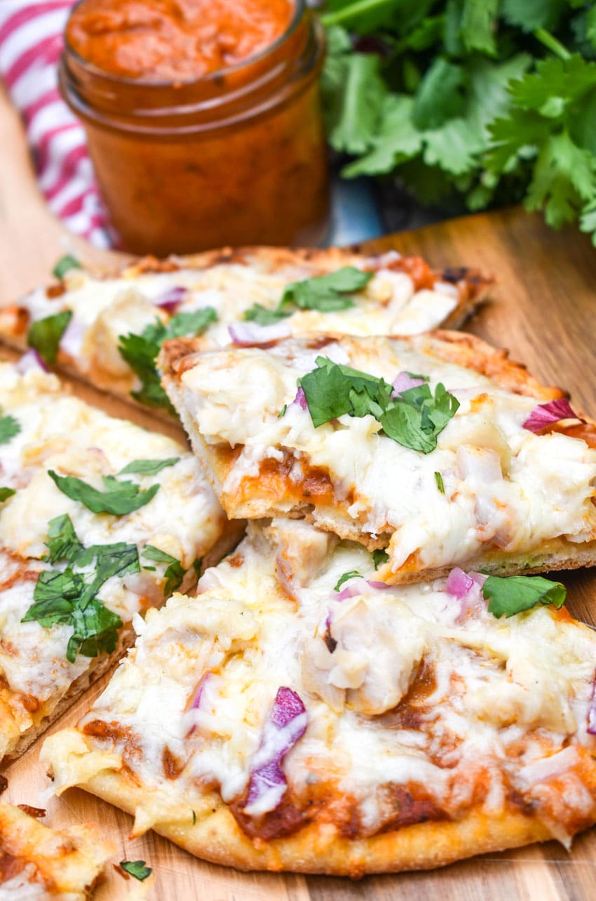 slices of chicken tikka masala pizza topped with fresh cilantro leaves on a wooden pizza peel