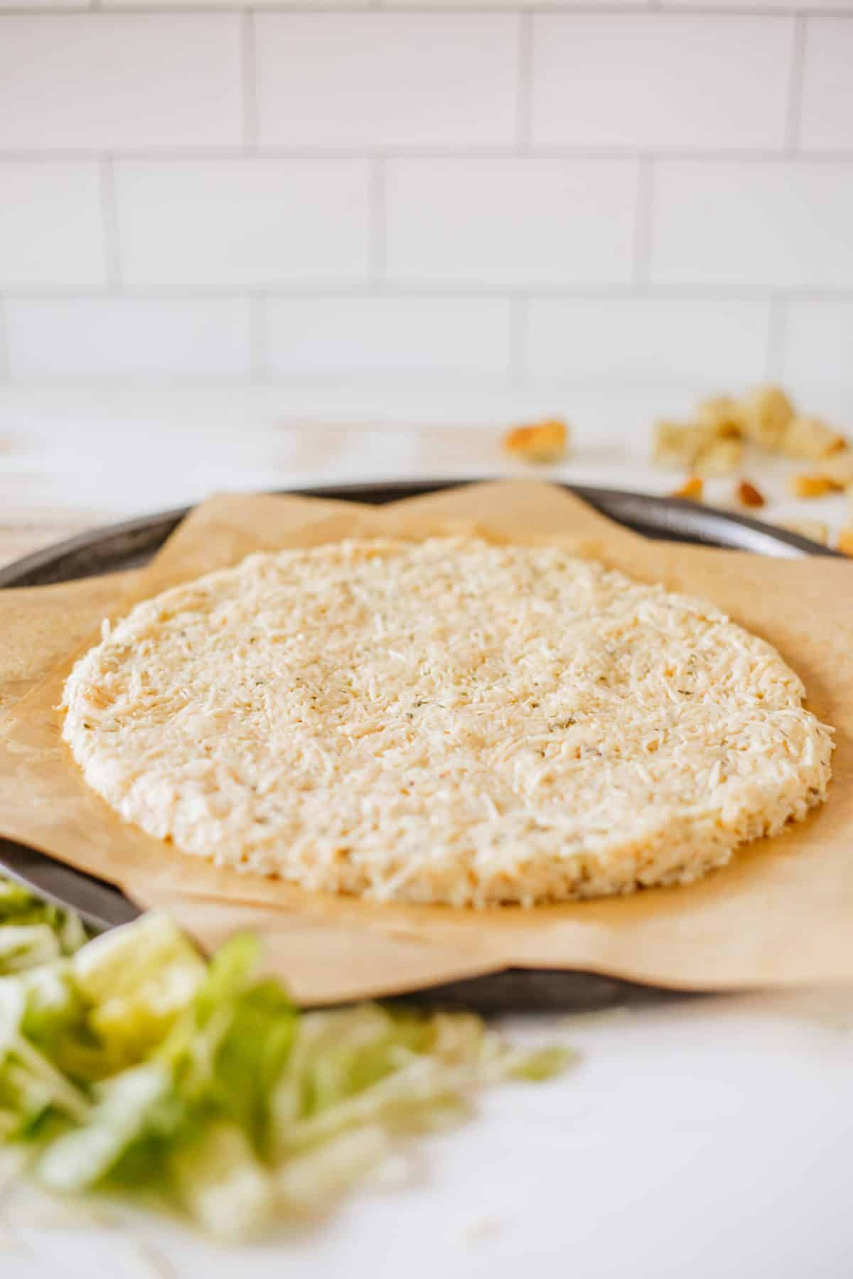 a homemade chicken pizza crust on a parchment paper lined baking sheet