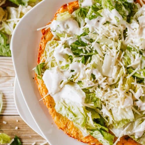 chicken caesar salad pizza on a white plate set on a wooden table