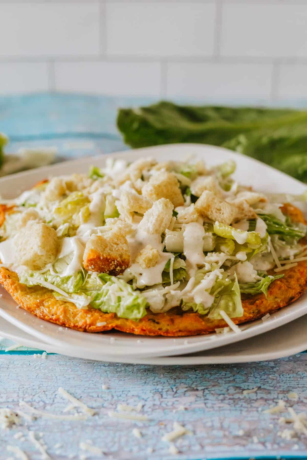 chicken caesar salad pizza on a white plate set on a wooden table