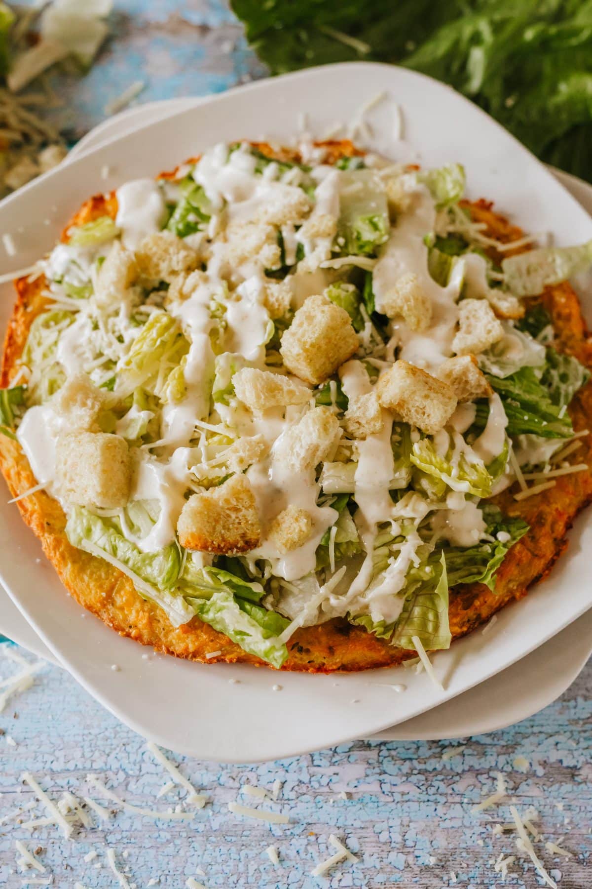 chicken caesar salad pizza on a white plate set on a wooden table
