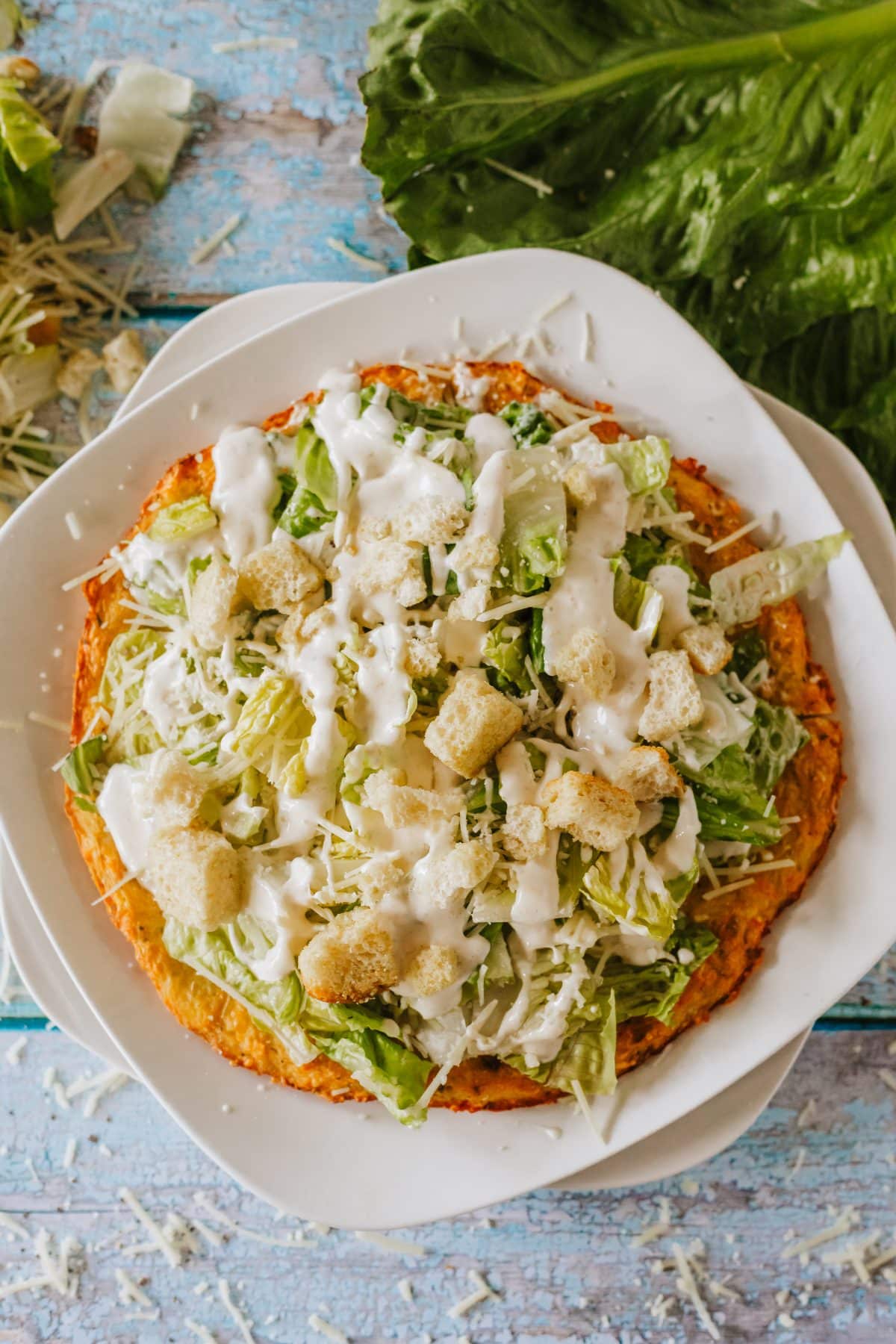 chicken caesar salad pizza on a white plate set on a wooden table