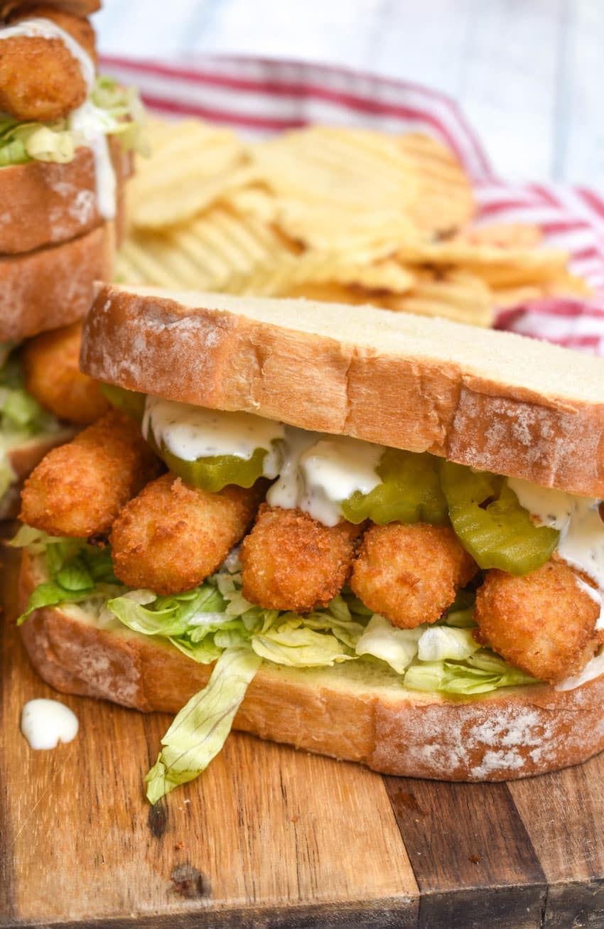 a fish finger sandwich on a wooden cutting board with potato chips in the background