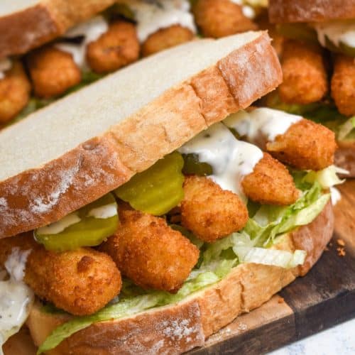 a fish finger sandwich on a wooden cutting board with potato chips in the background