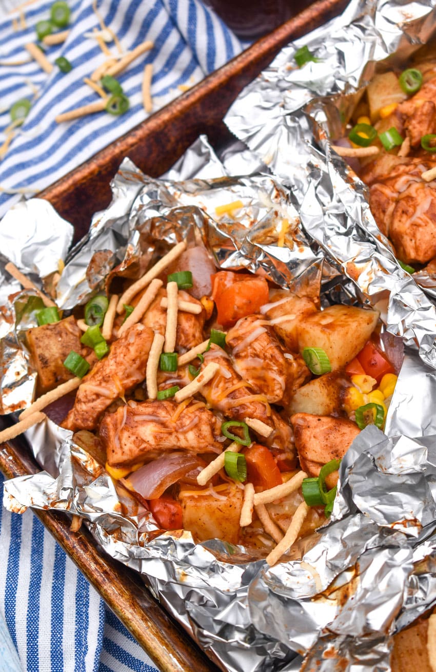 BARBECUE CHICKEN FOIL PACKETS OPENED ON A RIMMED METAL BAKING SHEET