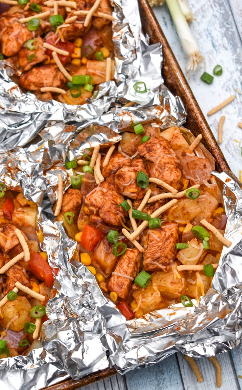 BARBECUE CHICKEN FOIL PACKETS OPENED ON A RIMMED METAL BAKING SHEET