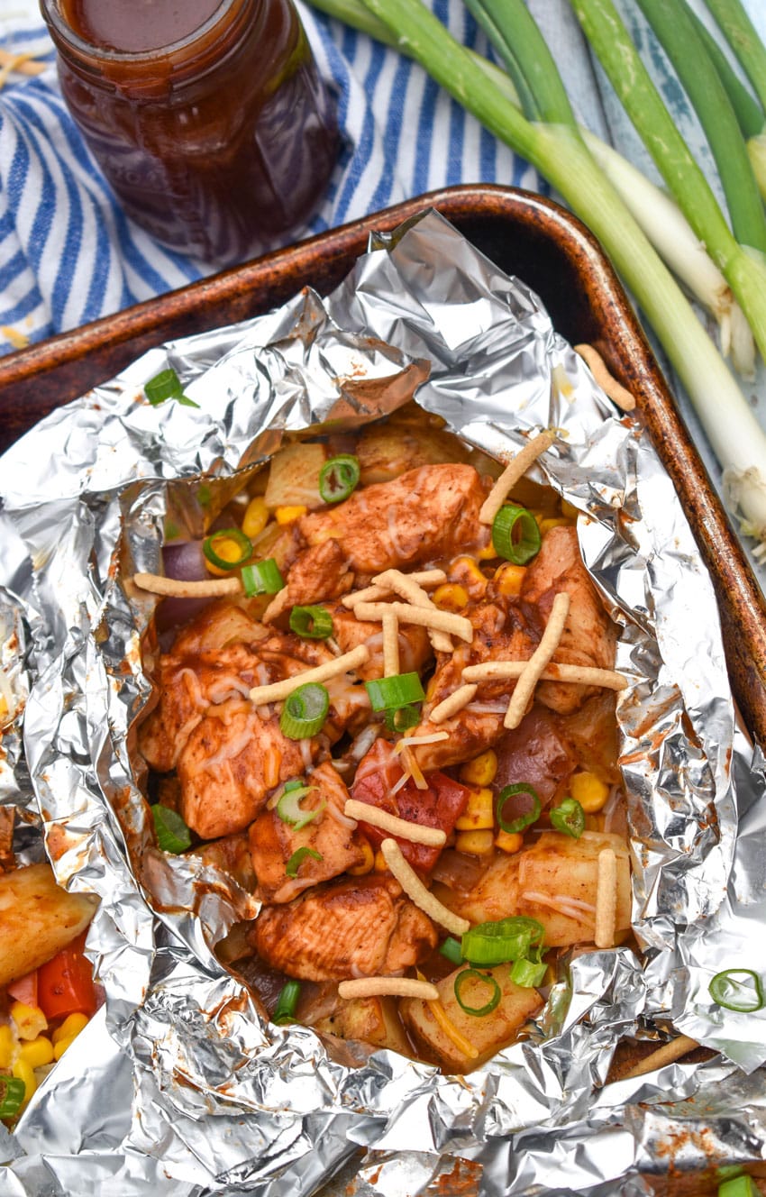 BARBECUE CHICKEN FOIL PACKETS OPENED ON A RIMMED METAL BAKING SHEET