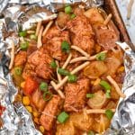 BARBECUE CHICKEN FOIL PACKETS OPENED ON A RIMMED METAL BAKING SHEET