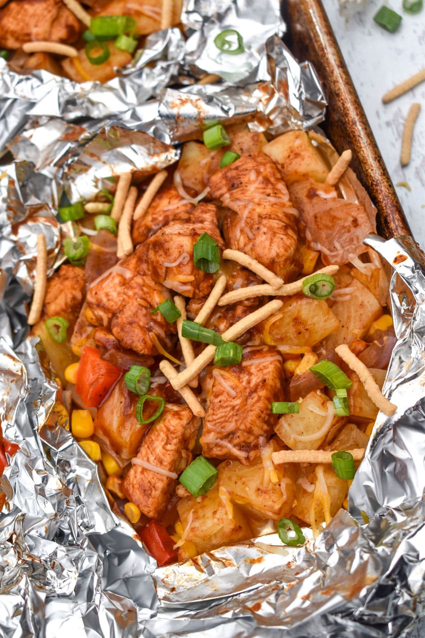 BARBECUE CHICKEN FOIL PACKETS OPENED ON A RIMMED METAL BAKING SHEET