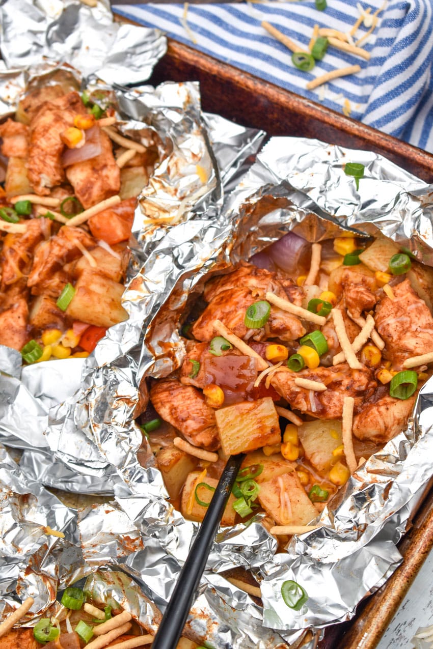 BARBECUE CHICKEN FOIL PACKETS OPENED ON A RIMMED METAL BAKING SHEET