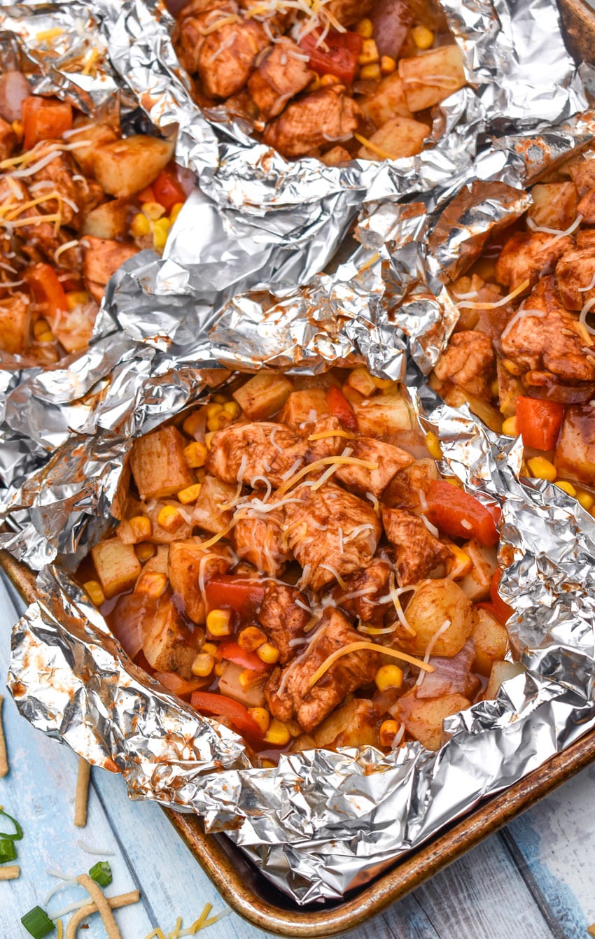 BARBECUE CHICKEN FOIL PACKETS OPENED ON A RIMMED METAL BAKING SHEET