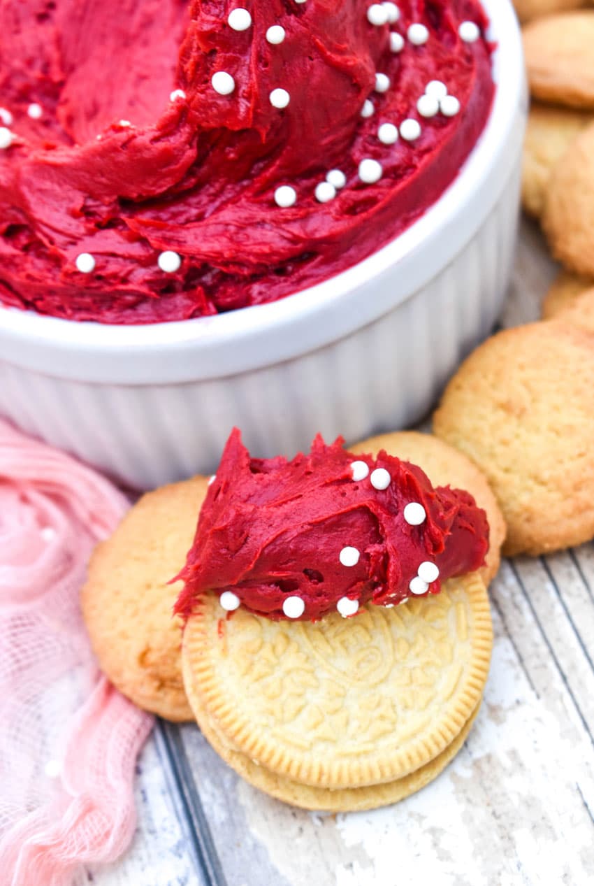 a golden oreo cookie topped with red velvet dip resting on a wooden table