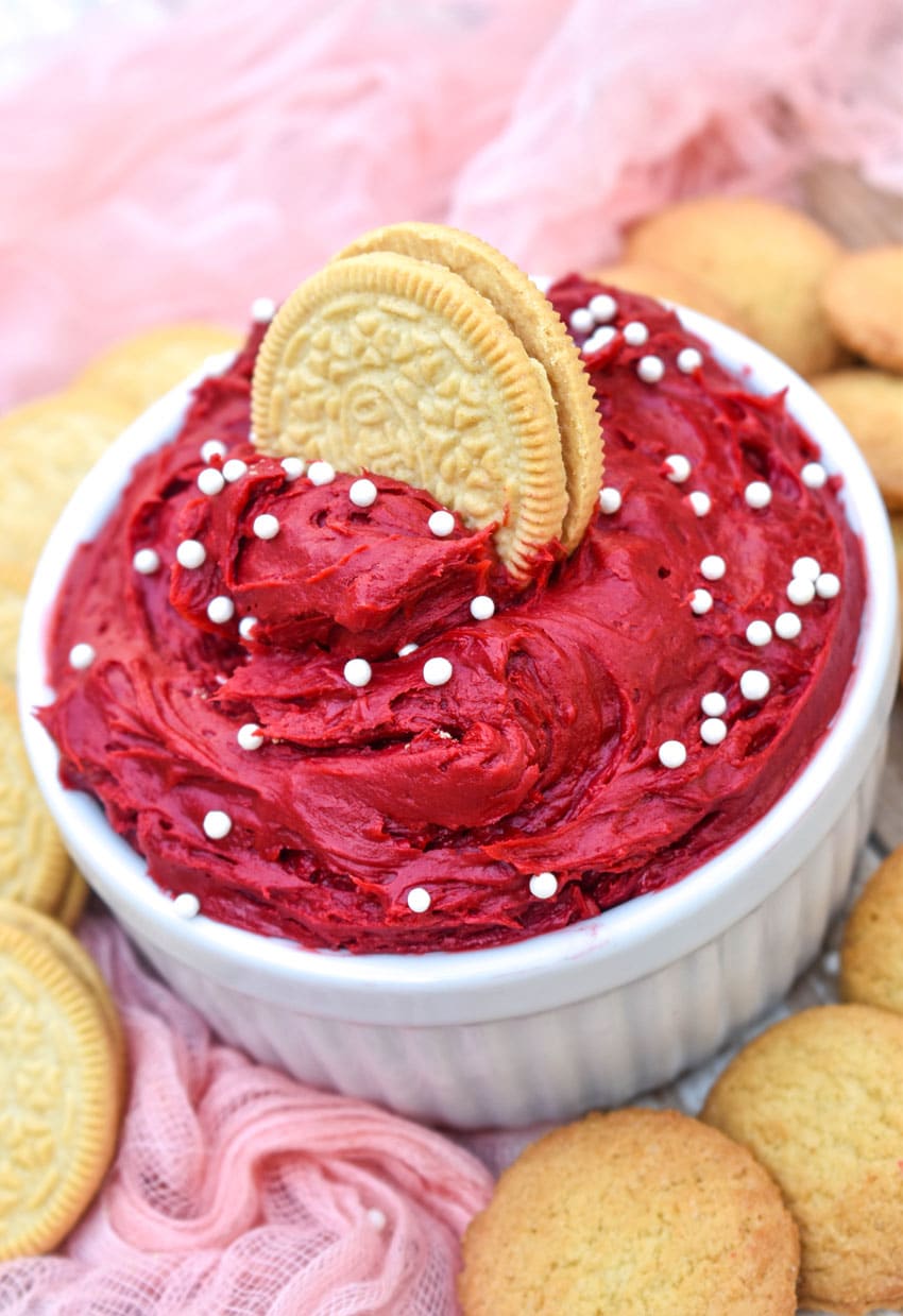 red velvet cake batter dip in a small white bowl surrounded by cookies