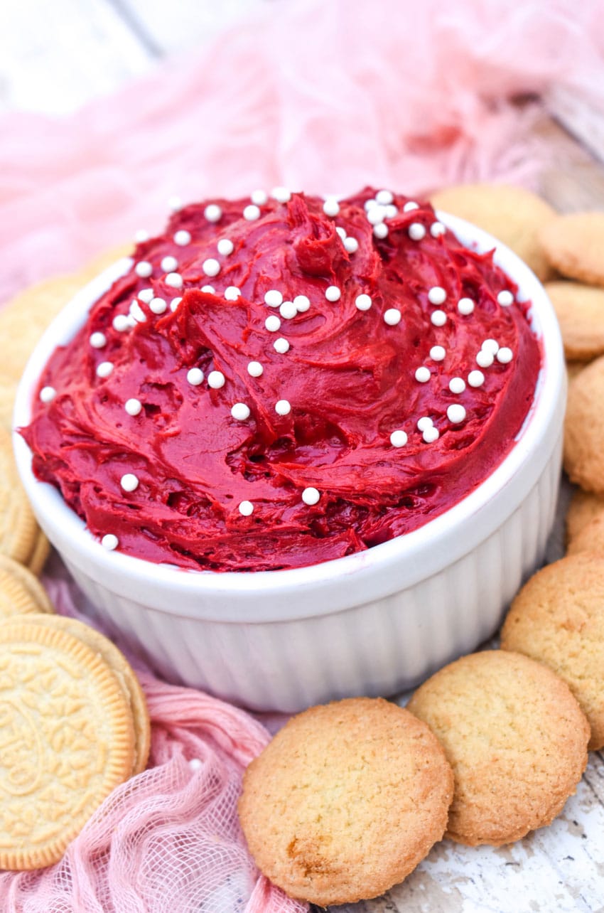 red velvet cake batter dip in a small white bowl surrounded by cookies