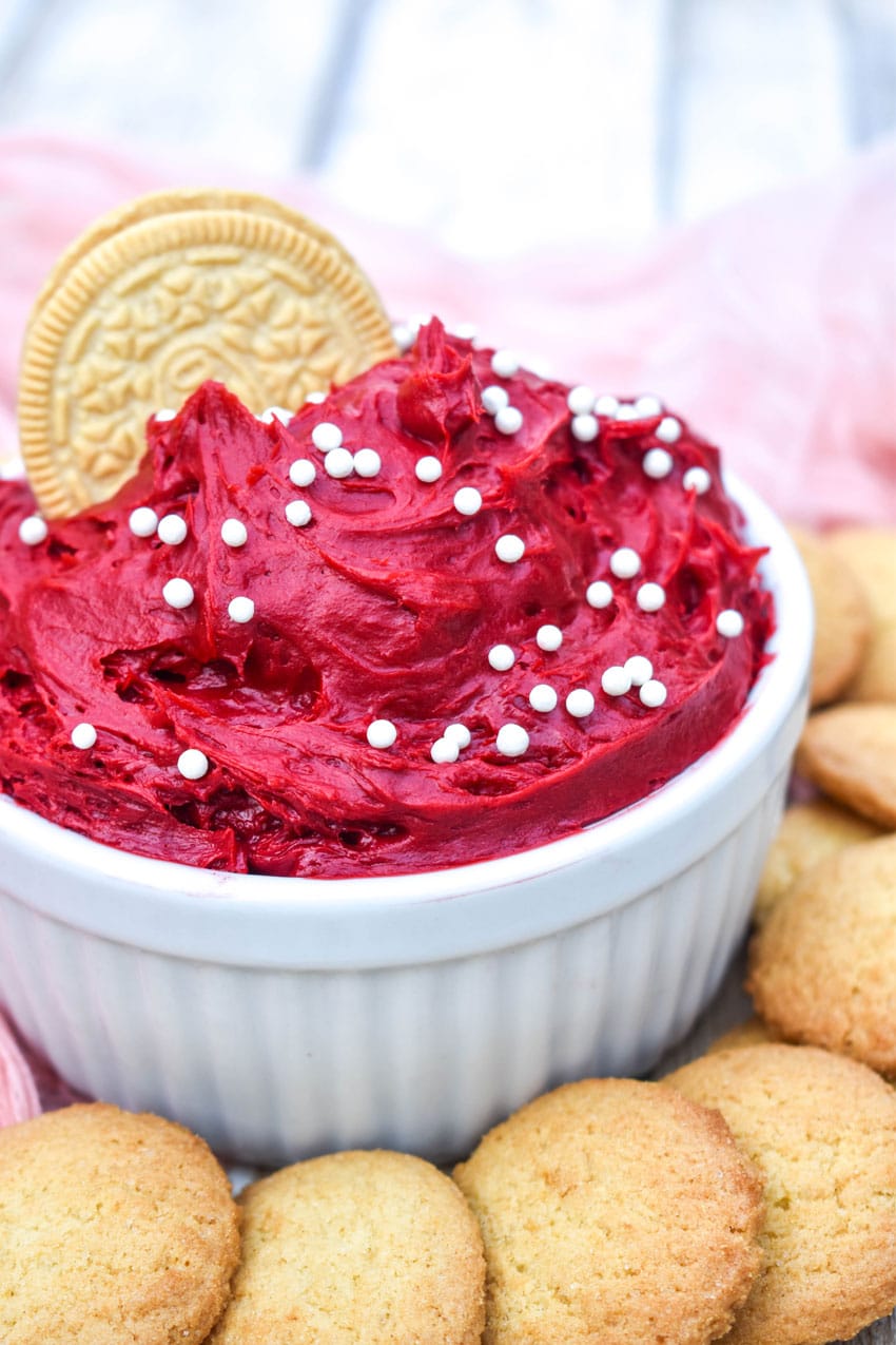 red velvet cake batter dip in a small white bowl surrounded by cookies