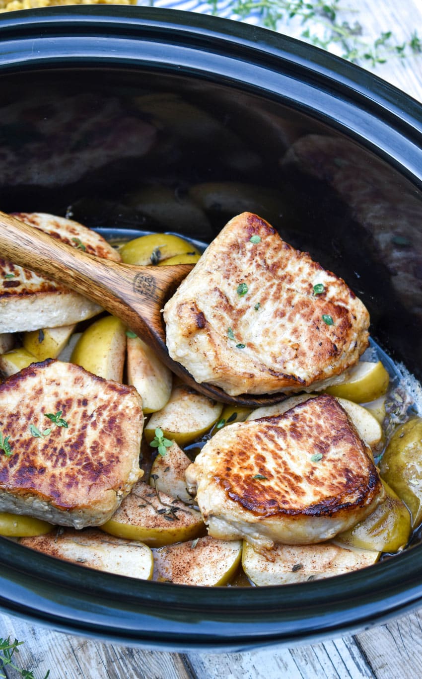 a wooden spoon scooping a pork chop out of a black crockpot