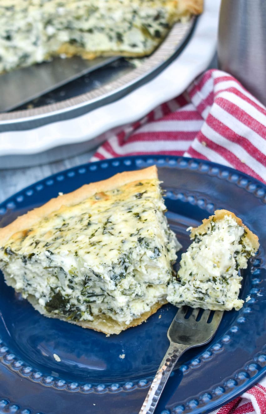 a slice of creamed spinach pie on a small blue plate with a silver fork resting on the side