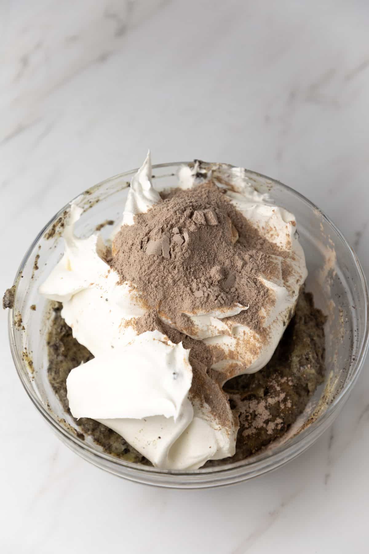 whipped topping being added to cookies and cream pudding in a glass mixing bowl