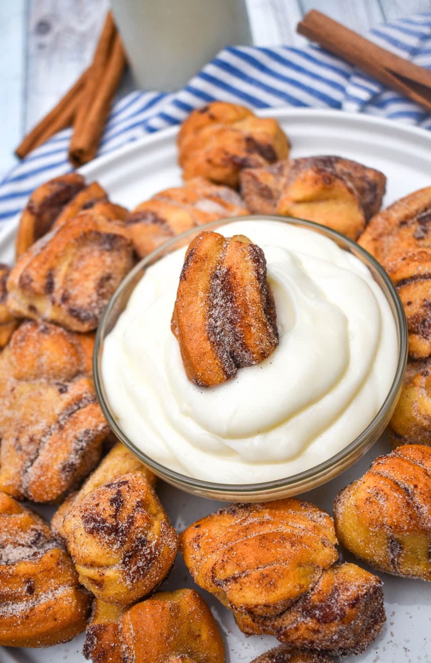 an air fryer cinnamon roll bite resting in a small bowl of cream cheese frosting