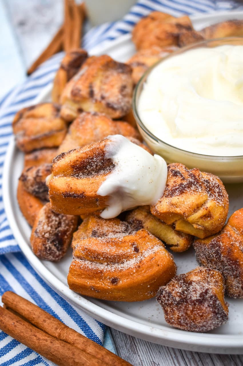 an air fryer cinnamon roll bite dipped in cream cheese frosting resting on a white plate