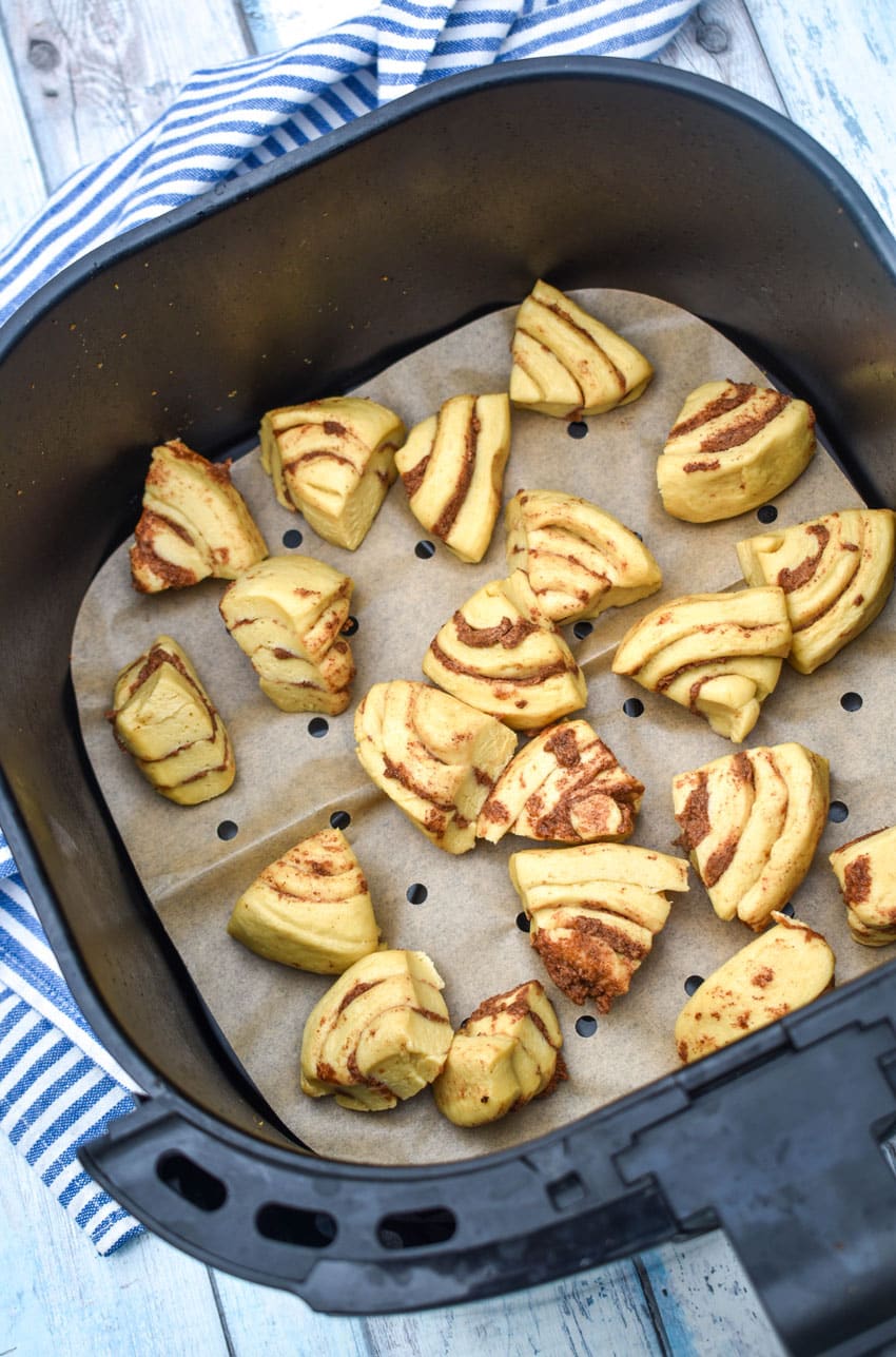 uncooked quartered cinnamon rolls in the basket of an air fryer
