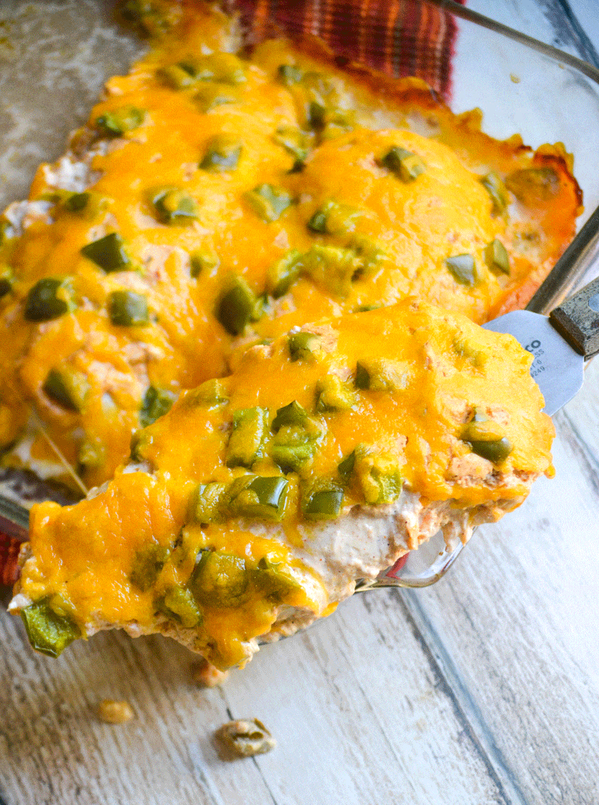 a spatula lifting a slice of baked cheesy fajita chicken out of a glass baking dish