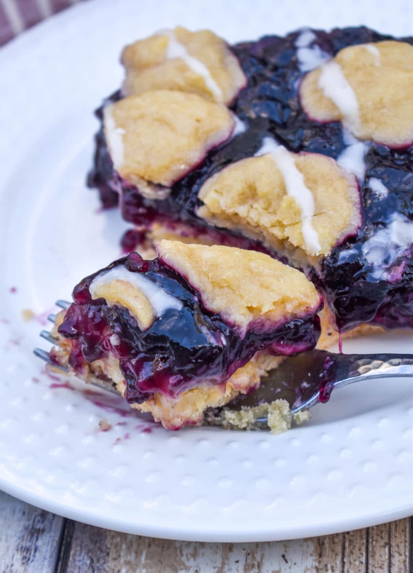 a silver fork holding a bite of blueberry pie bar resting on the edge of a small white plate