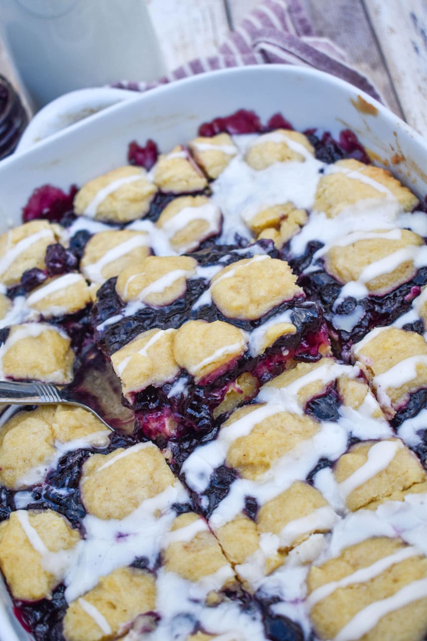 a silver spatula lifting a blueberry pie bar out of a white baking dish