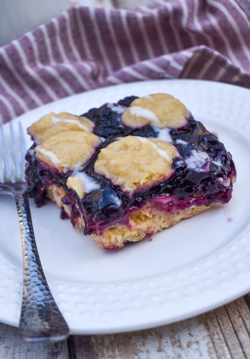a blueberry pie bar on a small white plate with a silver fork resting on the side